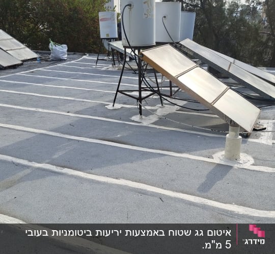 קווים לבנים של איטום על גג שטוח עם קולטי שמש